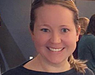 Close up photo of Amanda, smiling into the camera, she has blond hair with a pair of sunglasses perched on her head and is wearing a blue and gray striped shirt.
