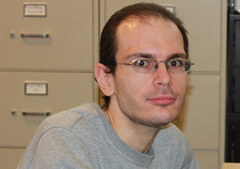 Paul sits at his desk with a computer, scanner, and filing cabinets behind him