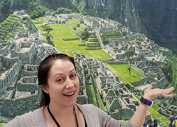photo of Alyson, smiling with her arms raised, in front of a poster-sized photo of Machu Picchu