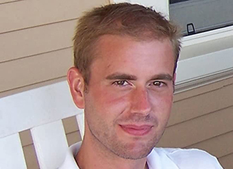 Close up photo of Benjamin seated on a portch. He has light brown hair and is wearing a white shirt with a collar.