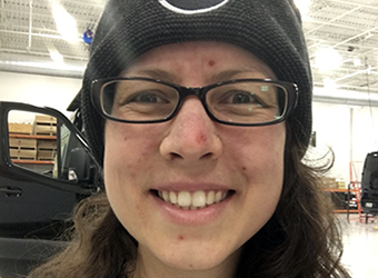 Close up photo of Emily wearing a knit hat and glasses smiling into the camera.