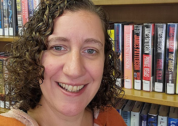 Photo of Kristin, smailing, in front of a library shelf full of books