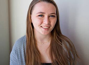 photo of Maggie, smiling, she has blue eyes, brown hair, and is wearing a gray sweater