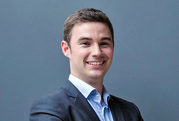 photo of Peter, grinning, with arms crossed, wearing a blue suit, but no tie, standing in front of a blue wall