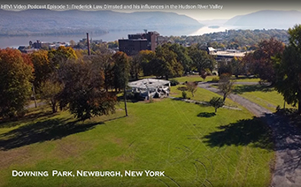 Aerial view of Downing Park showing grass, trees, and a gazebo in the foreground, brick buildings and house rooftops in the midground, and Newburgh Bay and the Hudson Highlands in the background.