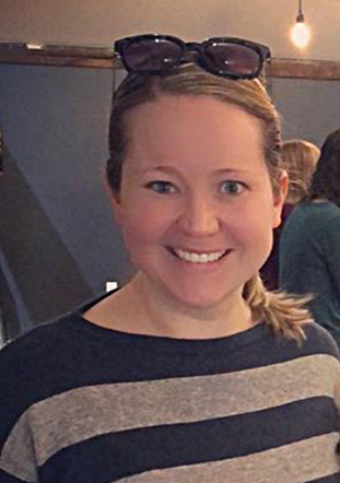 close up photo of Amanda, smiling into the camera, she has blond hair with a pair of sunglasses perched on her head and is wearing a blue and gray striped shirt.