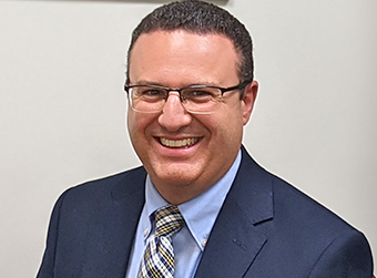 Phboto of Dan, smiling, wearing a blue coat and plaid tie.