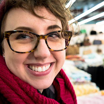 close up photo of Margot smiling into the camera. She is wearing tortoise shell glasses, and a fuschia scarf.