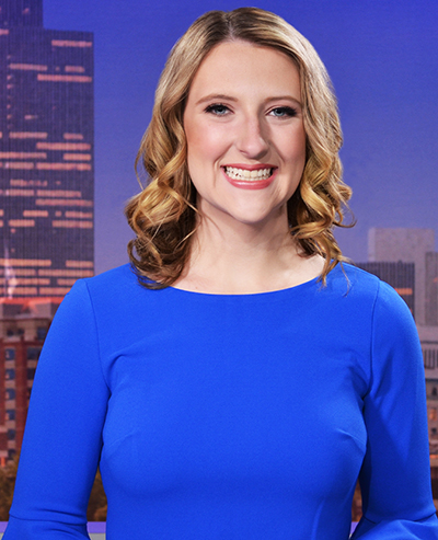 Young woman with blond hair, smiling, with a photo of the Empire State Plaza in the background on the set of the NewsChanel 13 studio
