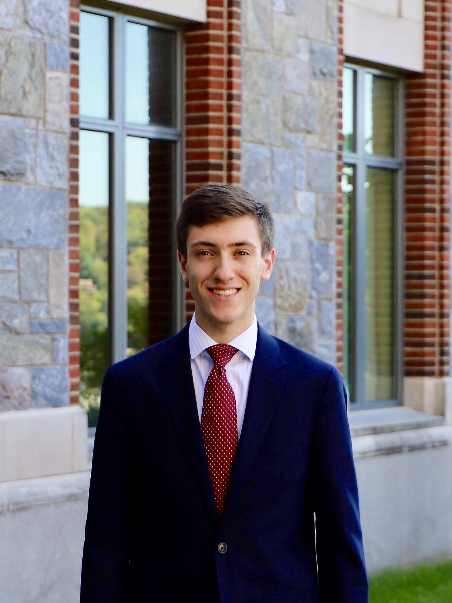 Spencer, standing in a suit and tie beside a stone and brick building on the Marist College campus.