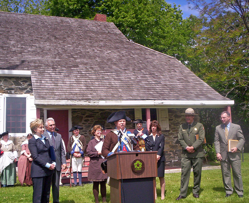 Photo of politicians and reeenactors in front of a historic stone house
