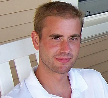 Photo of Benjamin, seated on a porch. He has light brown hair and is wearing a white whirt with a collar. 