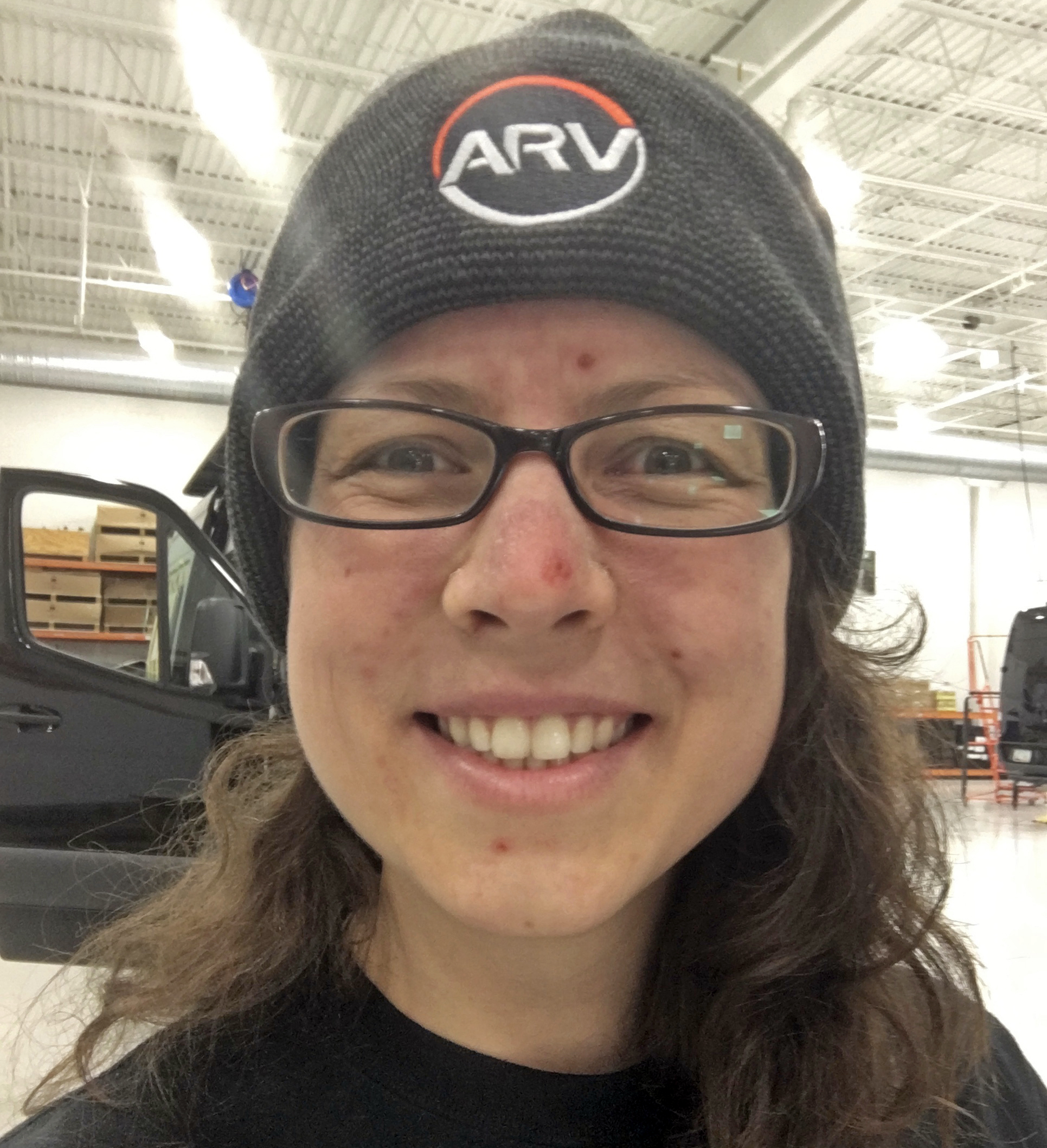 Close up photo of Emily wearing a knit hat and glasses smiling into the camera.