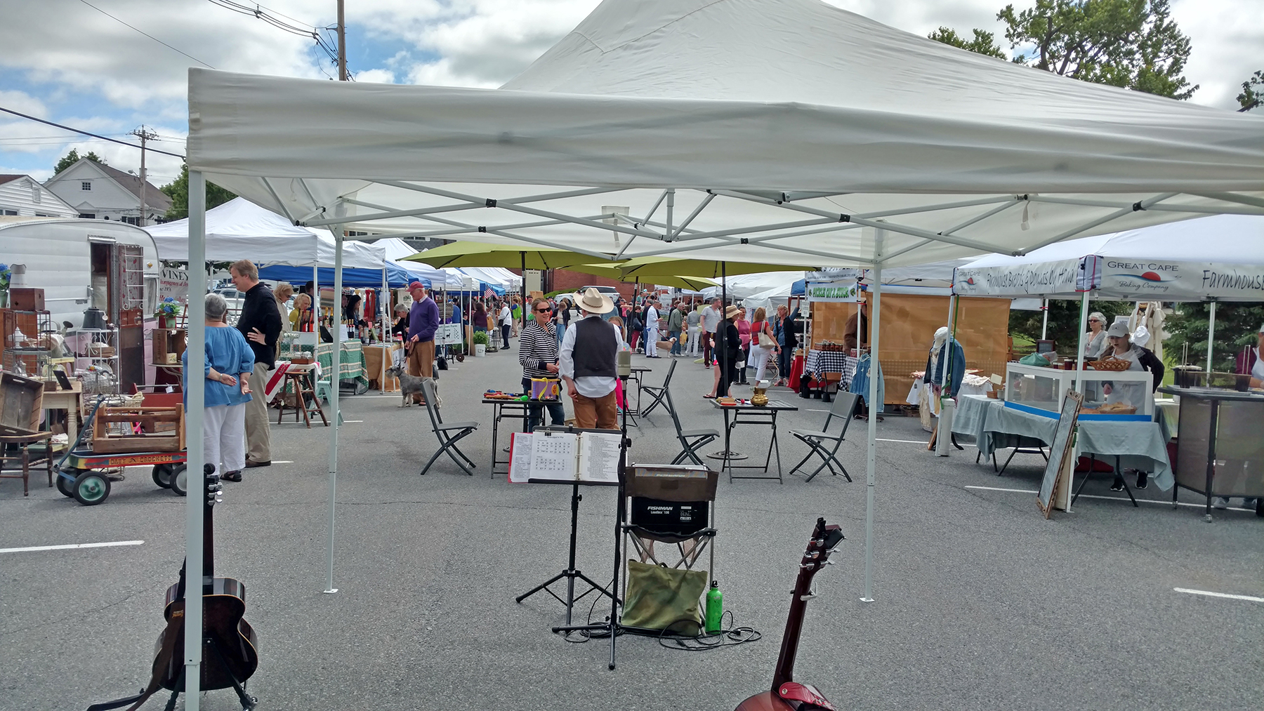 Photo of outdoor market showing a music tent as well as multiple vendor tents with people shopping