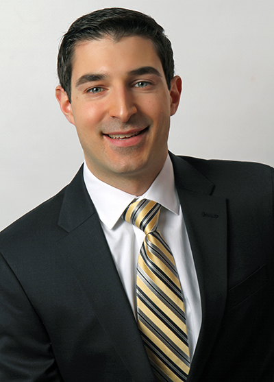 close up of Jason (black hair, blue eyes, smiling) in a black coat, white shirt, and yellow and gray striped tie